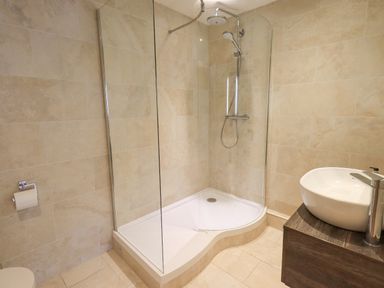 A bathroom with a corner shower enclosure a white sink on a wooden vanity and a toilet paper holder at Yew Cottage in Backbarrow