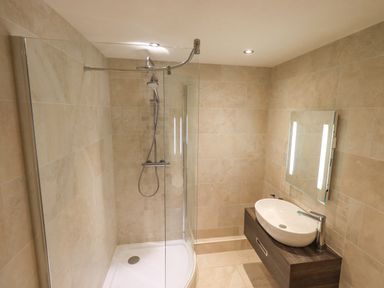 A bathroom with a shower enclosure and a sink with a mirror at Yew Cottage in Backbarrow