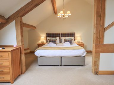 A bedroom with a double bed side tables lamps and wooden beams at Yew Cottage in Backbarrow
