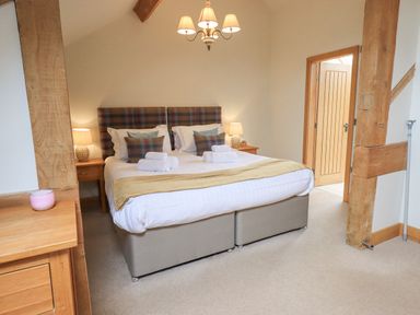 A bedroom with a double bed cushions bedside tables lamps wooden beams and an open door at Yew Cottage Backbarrow