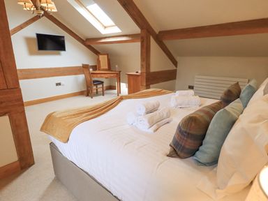 A bedroom with a bed with pillows and towels a desk and chair under a skylight at Yew Cottage in Backbarrow