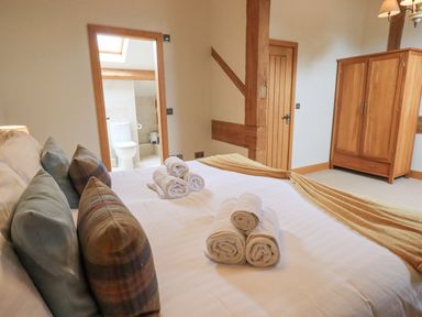 A bedroom with a bed towels and pillows with a wooden wardrobe and door at Yew Cottage in Backbarrow