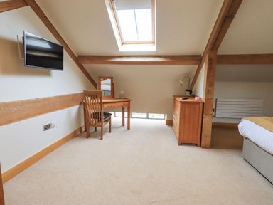 A bedroom with a desk and chair a dresser a wall-mounted television and a skylight window at Yew Cottage in Backbarrow