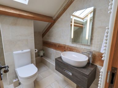 A bathroom with a toilet sink mirror and wooden beams at Yew Cottage in Backbarrow