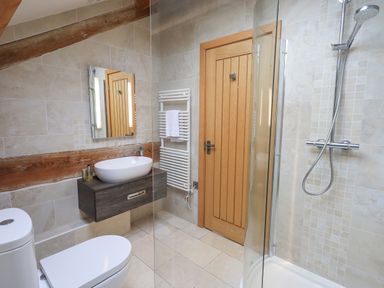 A bathroom with a toilet sink mirror wooden door towel radiator and a shower at Yew Cottage in Backbarrow
