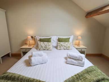 A bedroom with a double bed with pillows and towels on it and bedside tables with lamps at Yew Cottage in Backbarrow
