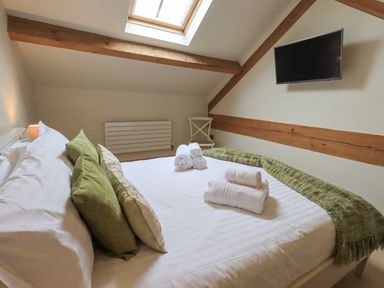 A bedroom with a bed with white linens green pillows and rolled white towels under a skylight at Yew Cottage in Backbarrow