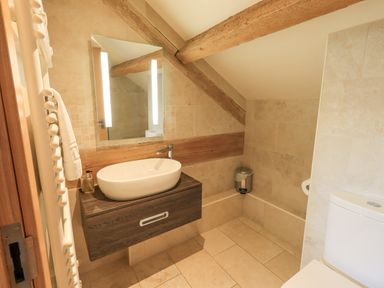 A bathroom with a sink cabinet mirror toilet and trash bin at Yew Cottage in Backbarrow