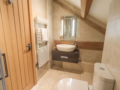 A bathroom with a toilet sink mirror wooden door towel rack and slanted ceiling at Yew Cottage in Backbarrow