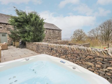 An outdoor hot tub next to a stone wall and a stone building with a green door at Yew Cottage in Backbarrow