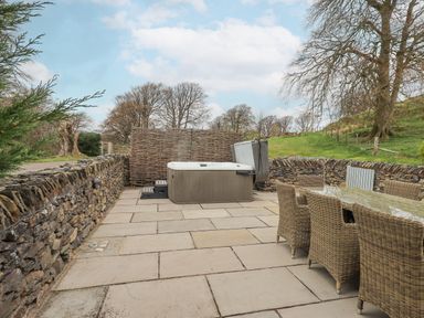 An outdoor patio area with a hot tub and wicker chairs around a glass table at Yew Cottage in Backbarrow