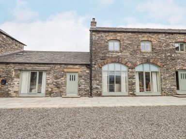 Stone exterior of a building with multiple green doors and windows with curtains at Lime Cottage in Backbarrow near Newby Bridge