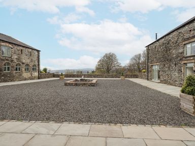 A gravel courtyard with a central stone water feature surrounded by stone buildings at Lime Cottage Backbarrow near Newby Bridge