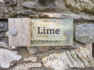 A stone wall with a glass and wood sign reading Lime Cottage at Lime Cottage in Backbarrow near Newby Bridge