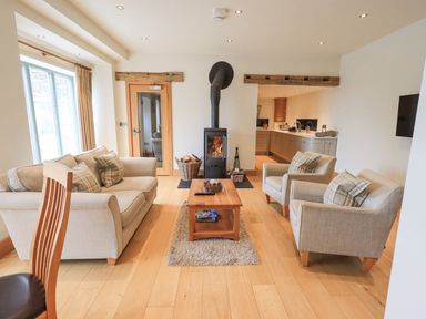 A living room with a wood stove sofa armchairs and a coffee table at Lime Cottage Backbarrow near Newby Bridge