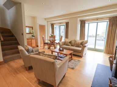 A living room with beige sofas a wooden coffee table glass dining table with chairs and stairs at Lime Cottage in Backbarrow near Newby Bridge