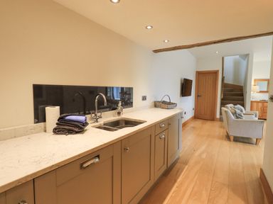 A kitchen with a sink and folded towels on the counter leading to a living area with chairs and a staircase at Lime Cottage in Backbarrow near Newby Bridge
