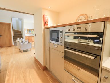 A kitchen area with microwave and oven and a living room with armchairs and stairs at Lime Cottage in Backbarrow near Newby Bridge