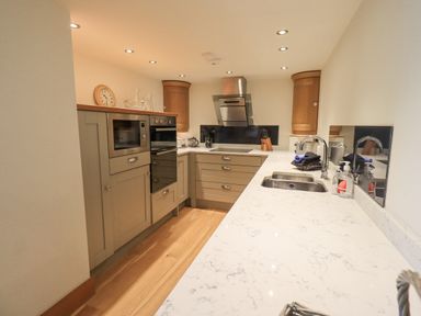 A kitchen with wooden cabinets a marble countertop a built-in microwave and oven and a stainless steel sink at Lime Cottage in Backbarrow near Newby Bridge