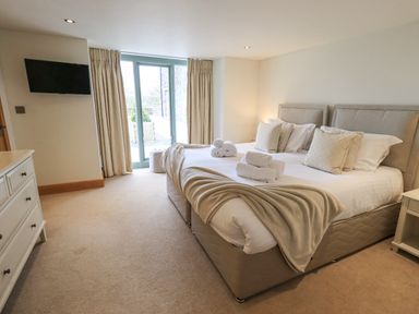 A bedroom with a double bed towels and blankets by a window with curtains and a wall mounted tv at Lime Cottage in Backbarrow near Newby Bridge