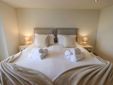 A bedroom with a double bed two side tables with lamps and rolled towels on the bed at Lime Cottage in Backbarrow near Newby Bridge