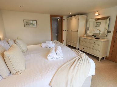 A bedroom with a bed with pillows and towels a wardrobe a dresser with a mirror and a door to a bathroom at Lime Cottage in Backbarrow near Newby Bridge