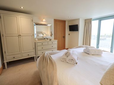 A bedroom with a bed with rolled towels a wardrobe dresser mirror wall mounted tv and sliding glass doors at Lime Cottage Backbarrow near Newby Bridge