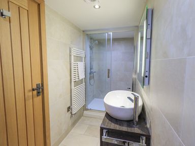 A bathroom with a wooden door a white towel radiator a glass shower enclosure and a white sink on a wooden cabinet at Lime Cottage Backbarrow near Newby Bridge