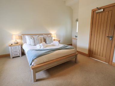 A bedroom with a bed pillows rolled towels lamps on bedside tables and a wooden door at Lime Cottage in Backbarrow near Newby Bridge