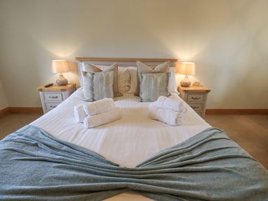 A bedroom with a bed covered with rolled towels and decorative pillows with bedside tables and lamps at Lime Cottage in Backbarrow near Newby Bridge