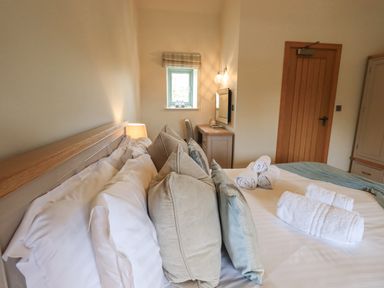 A bedroom with a bed with pillows and rolled towels a wooden door a window and a desk at Lime Cottage in Backbarrow near Newby Bridge