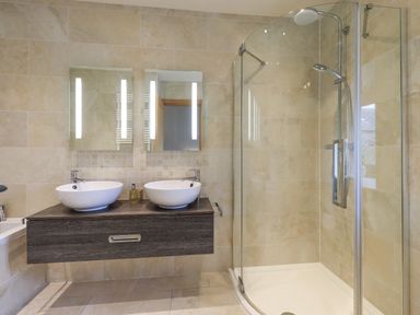 A bathroom with double sinks and a glass shower enclosure at Lime Cottage in Backbarrow near Newby Bridge