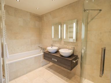 A bathroom with a bathtub double sinks mirrors and a glass shower enclosure at Lime Cottage in Backbarrow near Newby Bridge