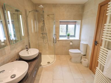A bathroom with two sinks a glass shower a toilet a window with a plant and a wooden door at Lime Cottage in Backbarrow near Newby Bridge