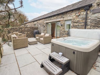 An outdoor patio area with a hot tub wicker seating set and a barbecue grill outside a stone cottage at Lime Cottage in Backbarrow near Newby Bridge