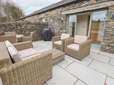 An outdoor patio with wicker seating and a covered grill at Lime Cottage in Backbarrow near Newby Bridge