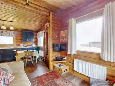 A wooden cabin interior with a kitchen area dining table and chairs a sofa and a window with curtains at Harbottle Lodge in Longframlington near Alnwick