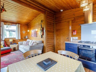An open living room and kitchen area with a sofa guitar and dining table at Harbottle Lodge in Longframlington near Alnwick