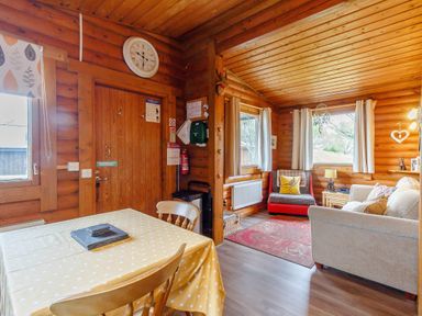 A dining area with a table and chairs next to a living area with a sofa and armchair in a wooden cabin at Harbottle Lodge in Longframlington near Alnwick