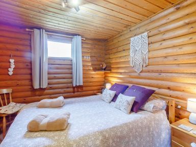 A bedroom with a bed covered with patterned bedspread and pillows in a wooden log cabin at Harbottle Lodge in Longframlington near Alnwick