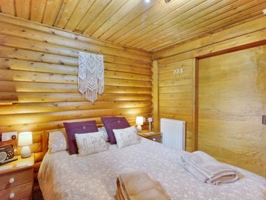 A bedroom with a double bed two bedside tables with lamps and wooden walls at Harbottle Lodge in Longframlington near Alnwick