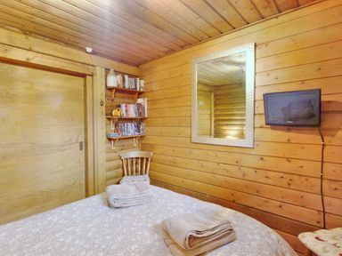 A bedroom with wood panel walls a bed with towels a chair shelves with books a mirror and a wall mounted tv at Harbottle Lodge in Longframlington near Alnwick
