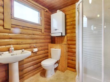 A bathroom with wooden walls a sink a toilet a water heater and a shower at Harbottle Lodge in Longframlington near Alnwick