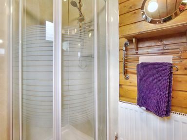 A shower with glass doors a towel rack with towels and a radiator in a wooden bathroom at Harbottle Lodge in Longframlington near Alnwick