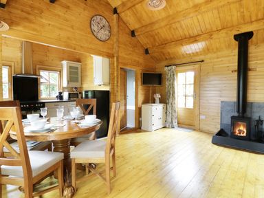 A wooden interior with a dining table set for four a kitchen area a wood burning stove and a TV at Acorn Lodge in Saxmundham