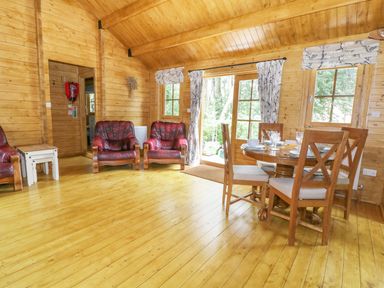 A wooden living room with three red leather armchairs a wooden dining table with four chairs and curtains on windows at Acorn Lodge in Saxmundham