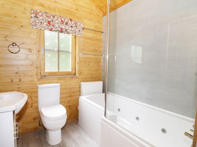 A bathroom with a toilet a sink a window and a bathtub with a shower screen at Acorn Lodge in Saxmundham
