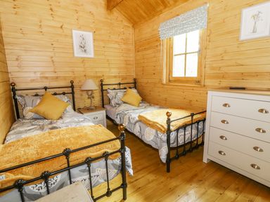 A bedroom with two single beds yellow pillows and a white dresser at Acorn Lodge in Saxmundham