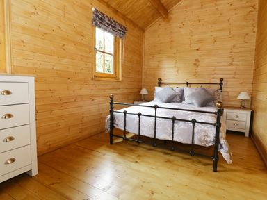 A bedroom with a black metal bed a white dresser and two white nightstands with lamps at Acorn Lodge in Saxmundham