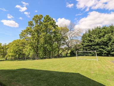 A grassy garden with a soccer goal and trees in the background at Foxes Meadow in Howey near Llandrindod Wells